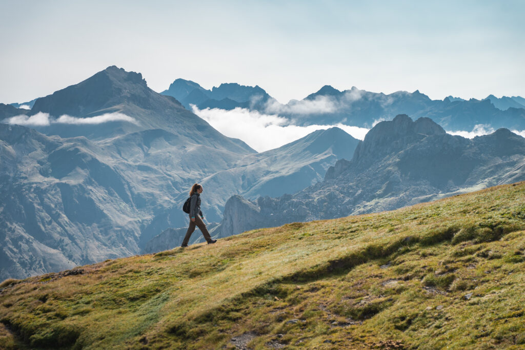 Woman walking up a grassy mound with mountains in the background