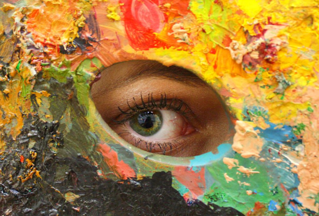 Eye peering through colourful palette hole.
