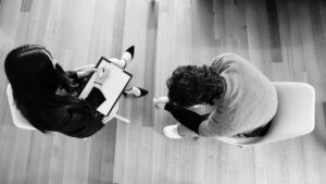 Woman listens to man and writes notes grayscale