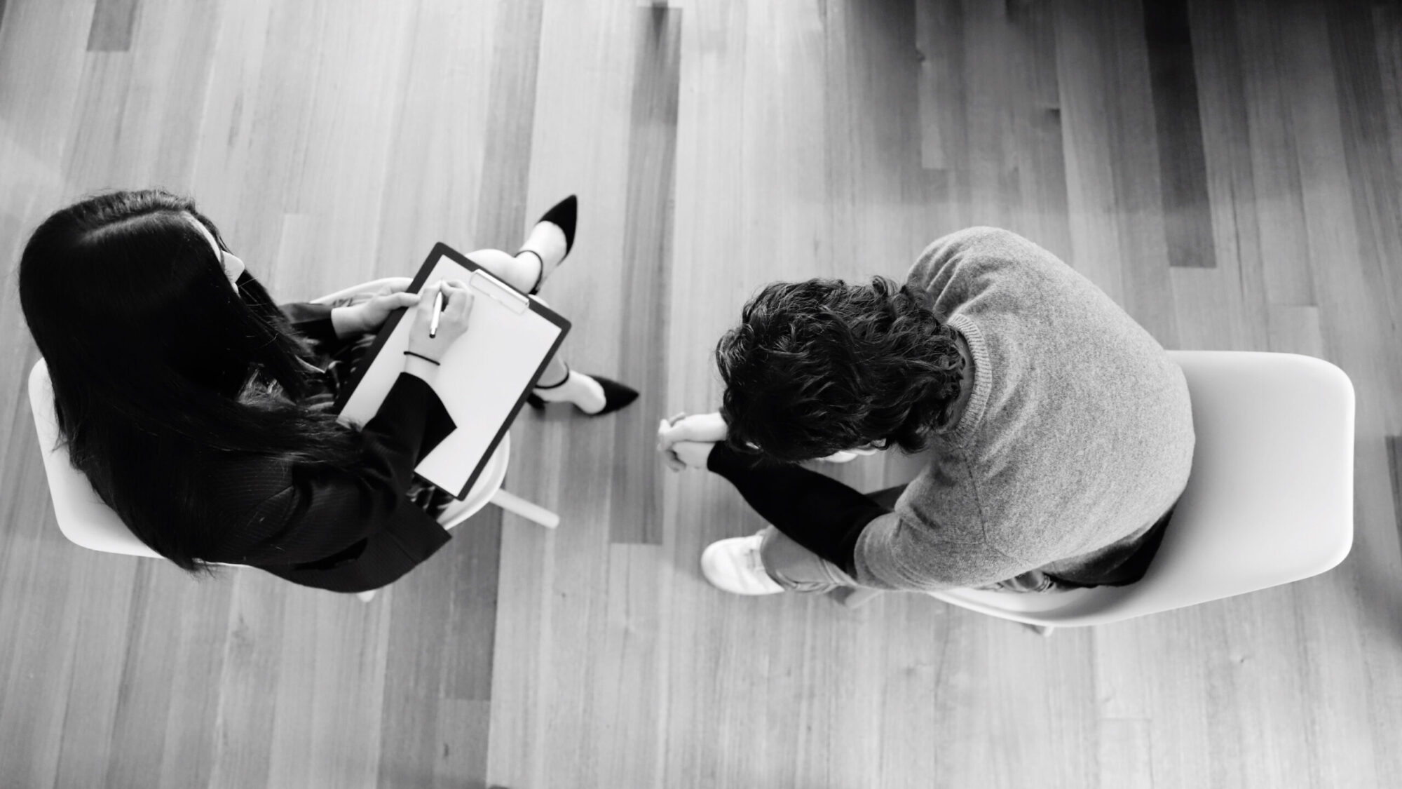 Woman listens to man and writes notes grayscale